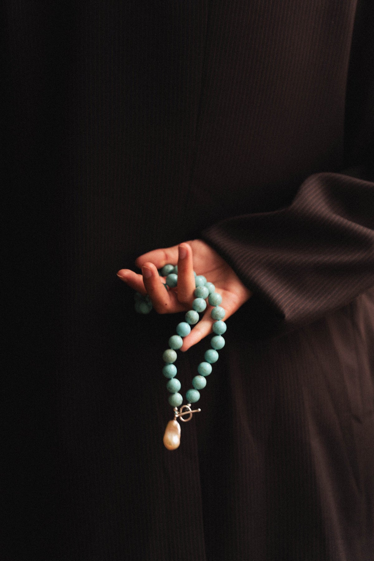Turquoise beaded necklace with a baroque pearl drop, held in the hand